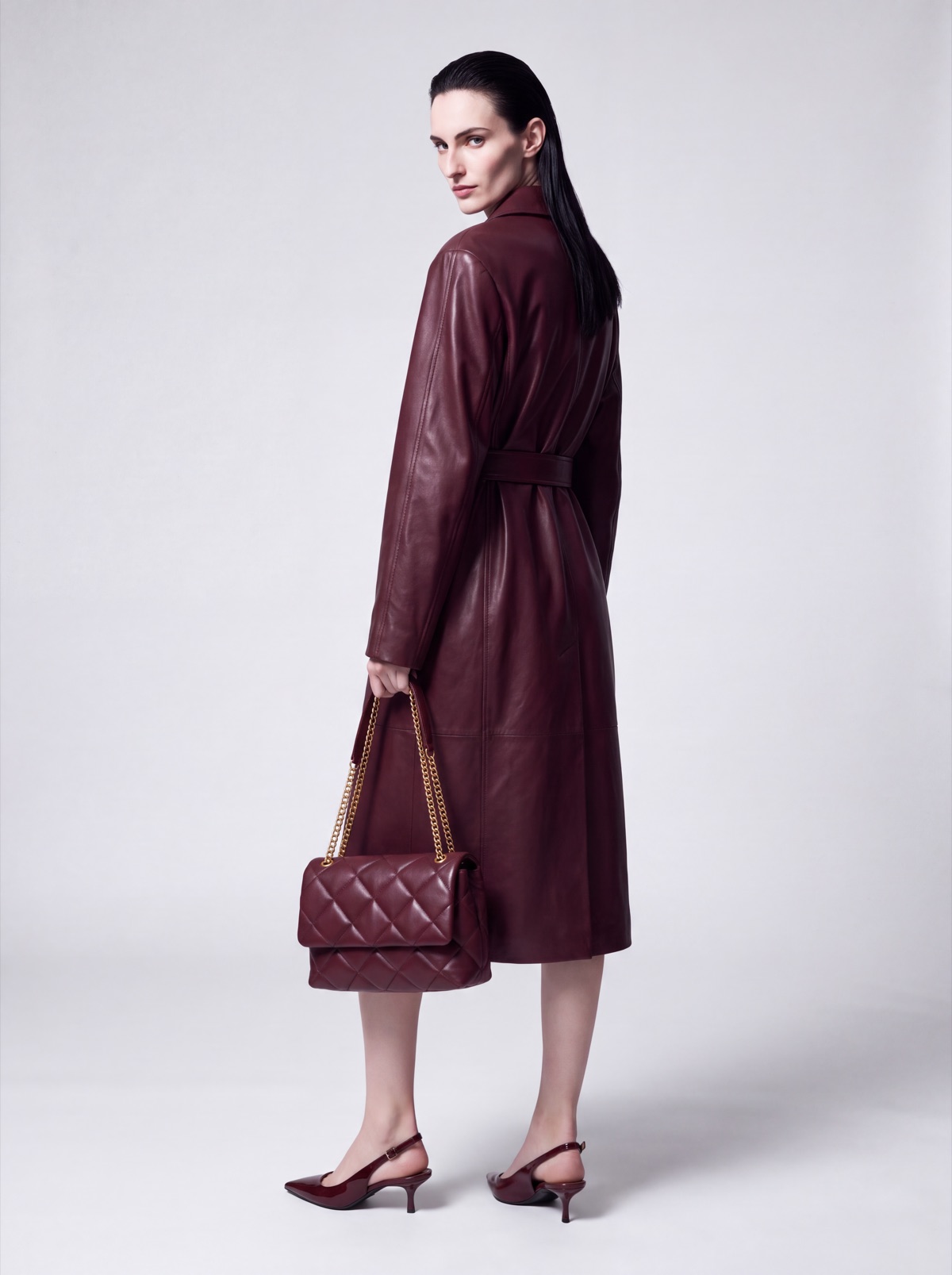 Burgundy leather trench coat and quilted bag on the same AI model, back view